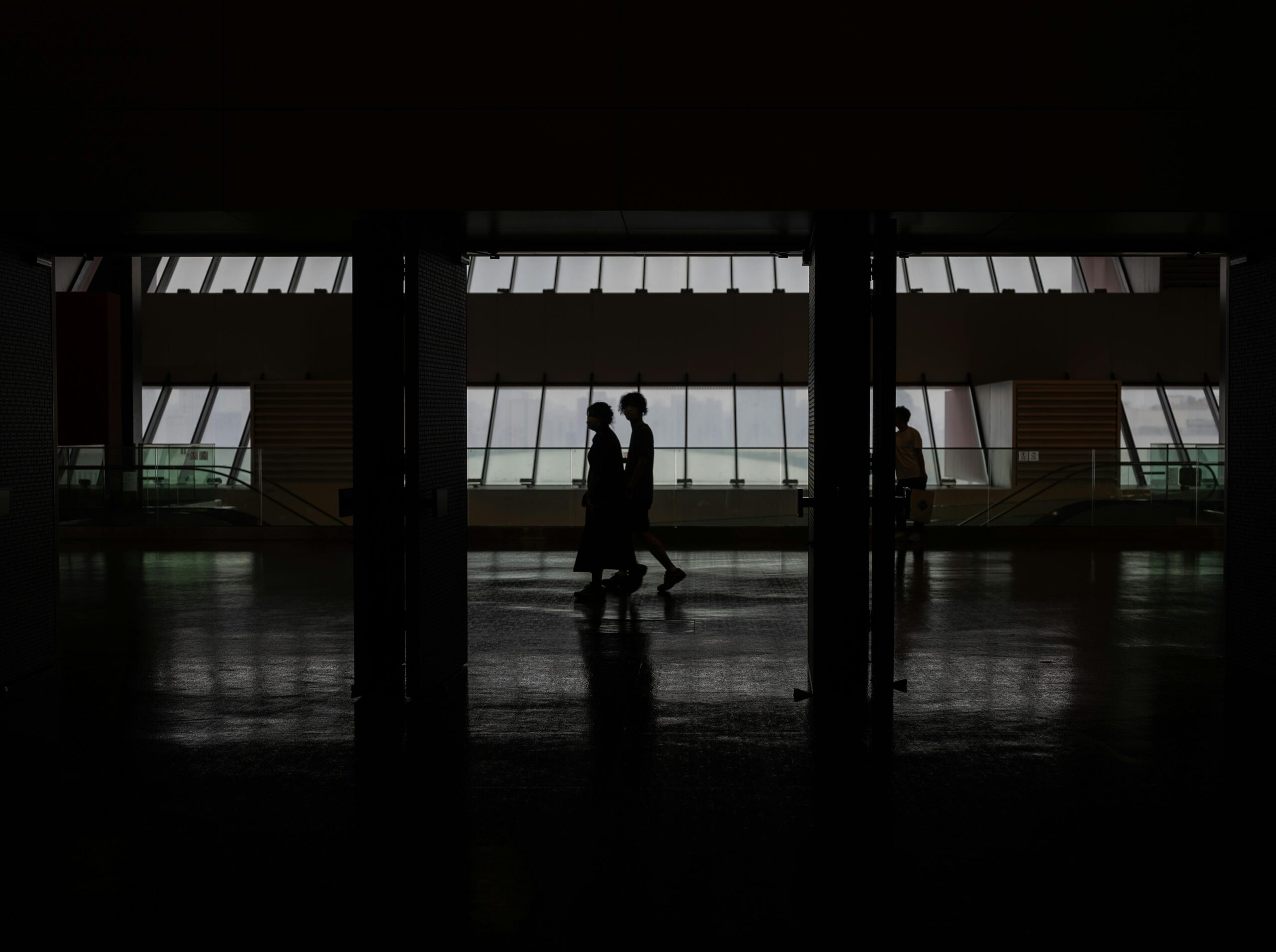 Blogs Silhouette of people walking through a modern hallway with large windows in Shanghai, China.