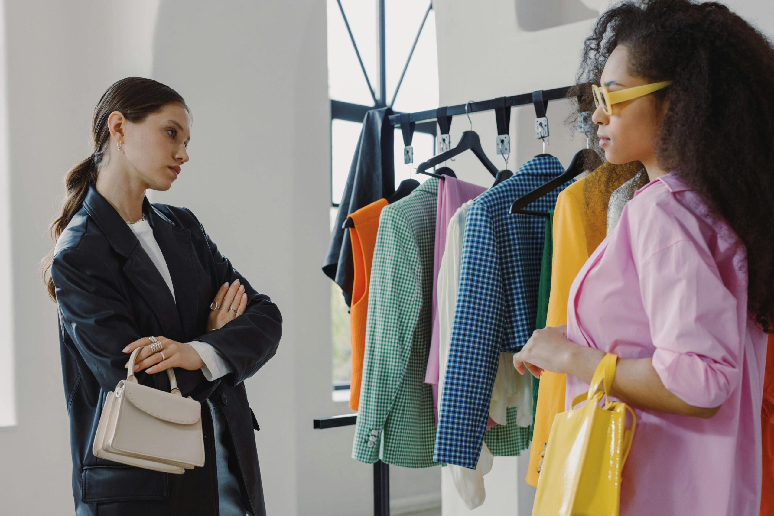 Home Two women browsing colorful clothing racks in a modern boutique.